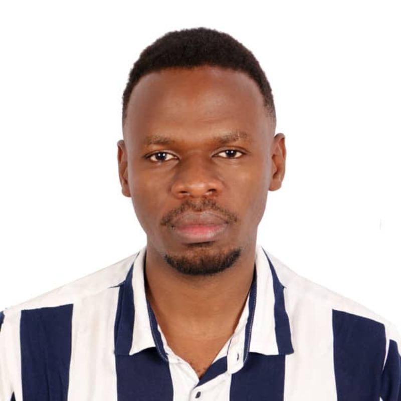 Deogracious Ssekono - SafePlace Internation A man with short hair and a trimmed beard wears a white shirt with bold black vertical stripes, facing the camera against a plain white background. SafePlace International