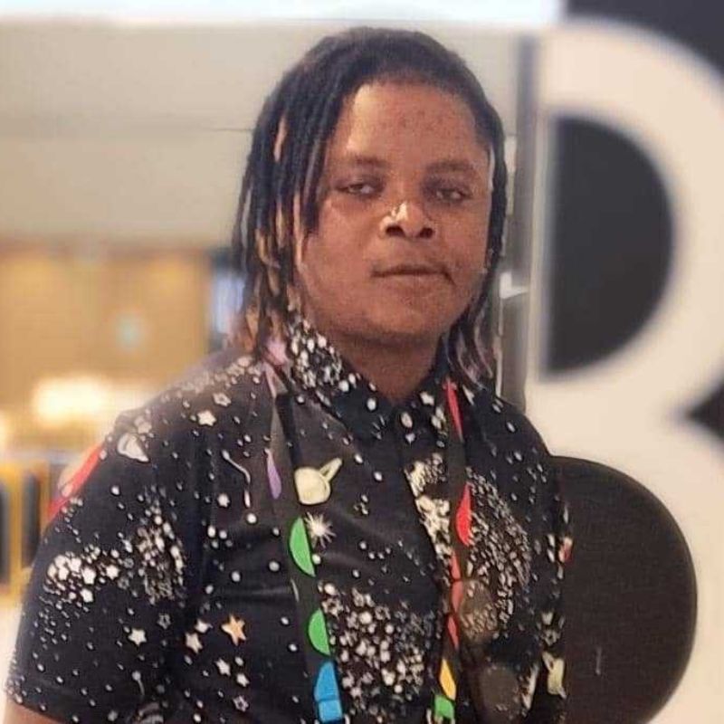 Elorm - SafePlace Internation A person with medium-length dreadlocks wears a black shirt with a colorful space-themed pattern, standing indoors with a blurred background. SafePlace International